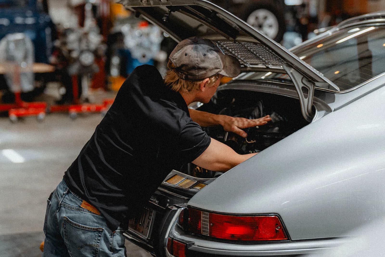 A technician working in the rear engine bay of a silver Porsche at Speed House