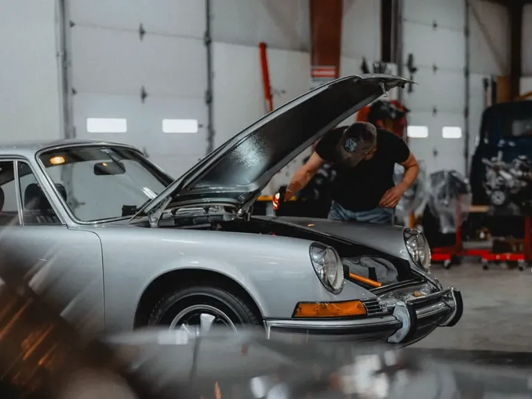 Technician inspecting a silver air-cooled Porsche in the Speed House workshop