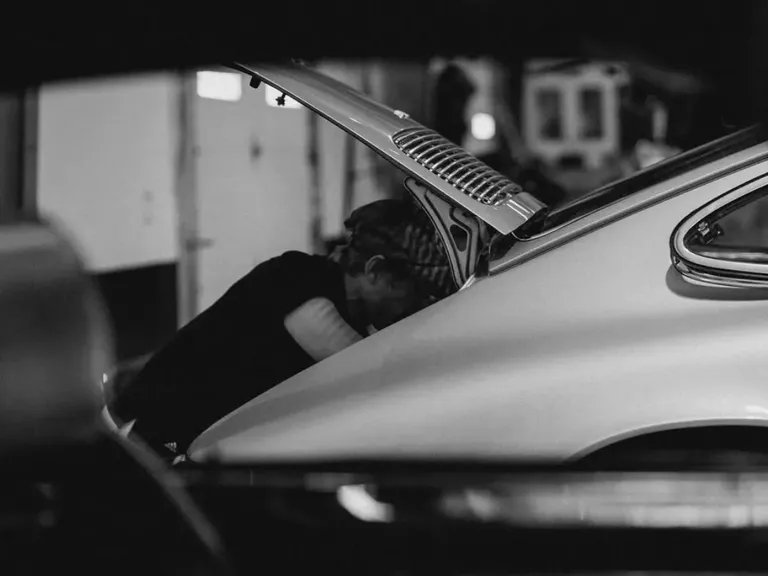 A person working at the open rear engine bay of a classic car